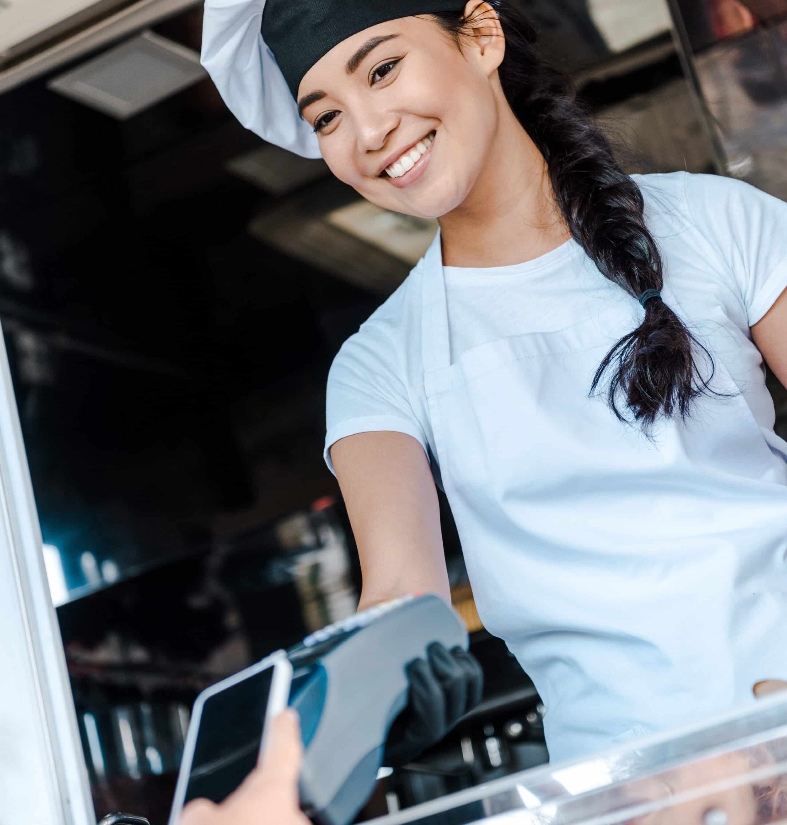 cropped view of woman paying with smartphone near asian girl in food truck